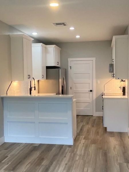 A contemporary kitchen features sleek white cabinetry and durable wood-look flooring. A contemporary kitchen features sleek white cabinetry and durable wood-look flooring.