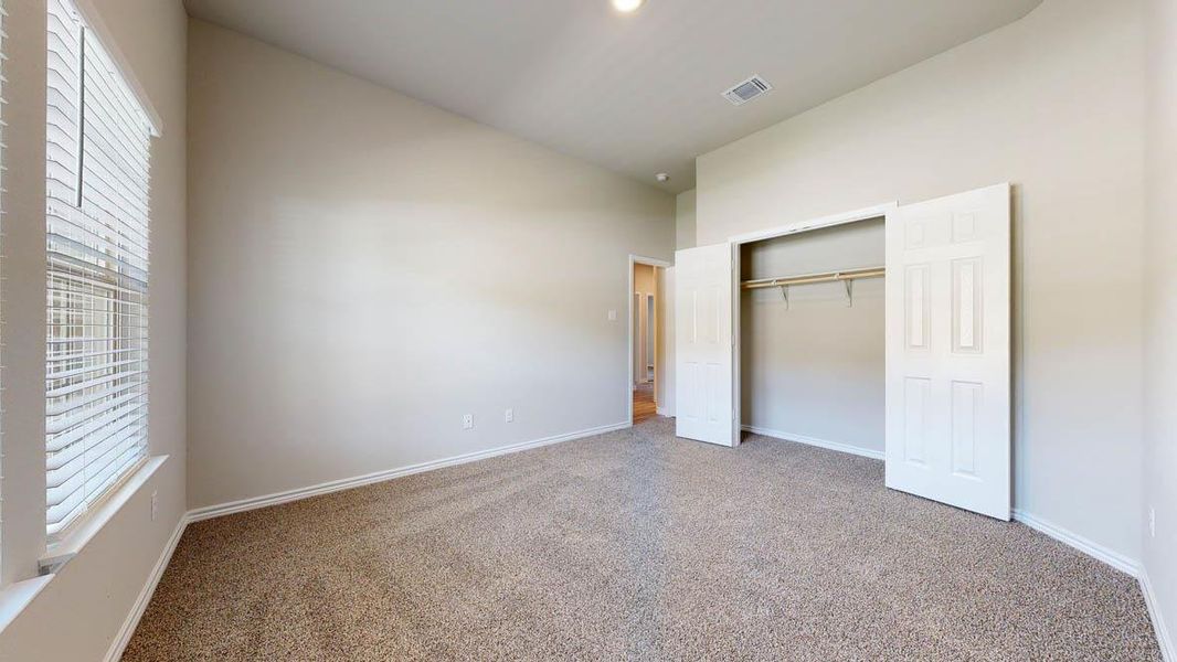 Spacious room featuring neutral carpet flooring, light-colored walls, a closet with bi-fold doors and built-in shelving, and a window with blinds