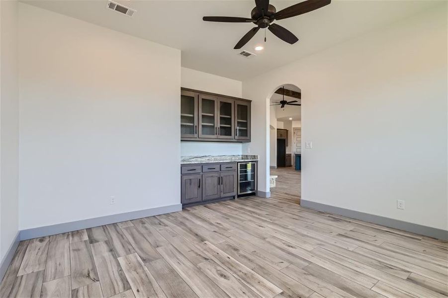 Unfurnished living room with wine cooler, light wood-type flooring, and ceiling fan