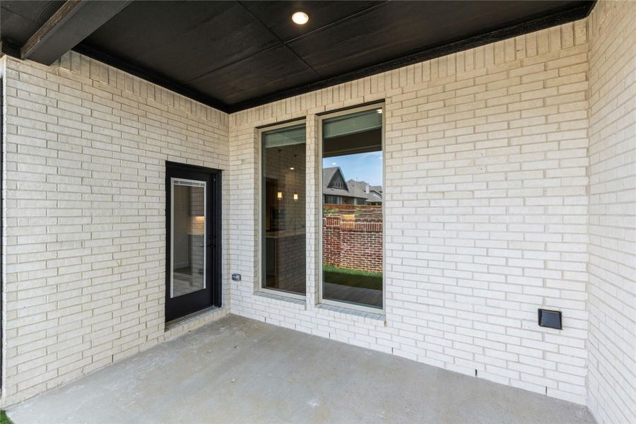 Covered back patio with white brick exterior, black door, and large windows on concrete slab