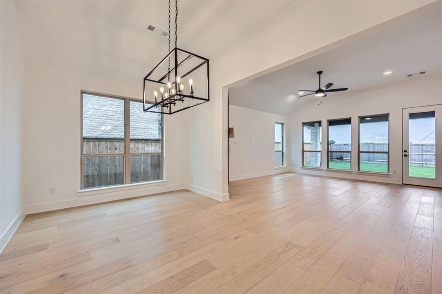 Unfurnished living room with ceiling fan with notable chandelier, vaulted ceiling, and light hardwood / wood-style flooring