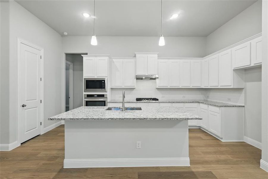 Kitchen featuring white cabinets, decorative light fixtures, light stone countertops, light wood finished floors, and appliances with stainless steel finishes Kitchen featuring white cabinets, decorative light fixtures, light stone countertops, light wood finished floors, and appliances with stainless steel finishes