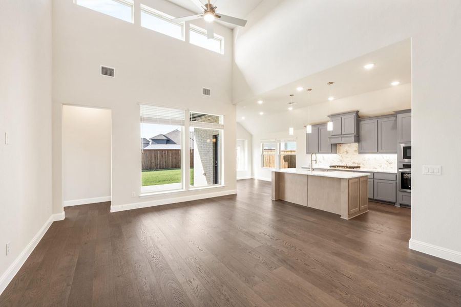 Open-concept living area with high ceilings, dark hardwood floors, and kitchen with gray cabinets and center island Open-concept living area with high ceilings, dark hardwood floors, and kitchen with gray cabinets and center island