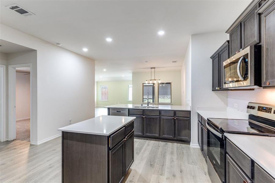Kitchen featuring wood-finish flooring, dark cabinetry, and white countertops Kitchen featuring wood-finish flooring, dark cabinetry, and white countertops