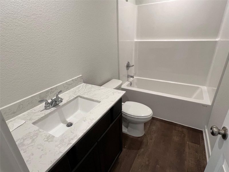 Bathroom with a textured wall, vanity, shower combination, and dark wood-type flooring Bathroom with a textured wall, vanity, shower combination, and dark wood-type flooring