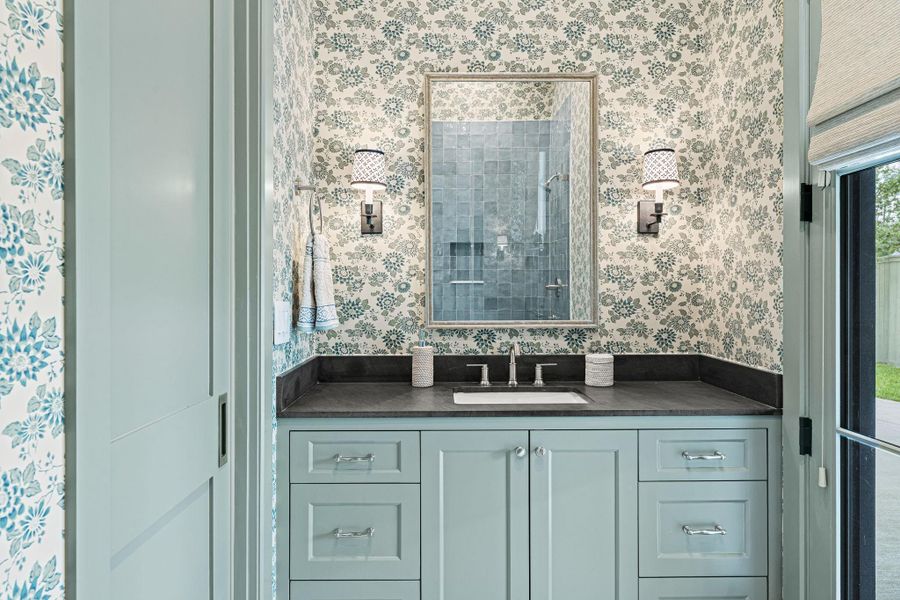 Well-appointed en suite bath for the first floor flex room featuring honed granite countertop, designer wallpaper & Visual Comfort sconces. A walk-in shower w/ frameless glass door, Zellige tile surround, soap niche & tumbled stone mosaic flooring creates a clean, elevated finish. A secondary door leads to the porte cochere, adding convenience & flexibility for everyday use. Well-appointed en suite bath for the first floor flex room featuring honed granite countertop, designer wallpaper & Visual Comfort sconces. A walk-in shower w/ frameless glass door, Zellige tile surround, soap niche & tumbled stone mosaic flooring creates a clean, elevated finish. A secondary door leads to the porte cochere, adding convenience & flexibility for everyday use.