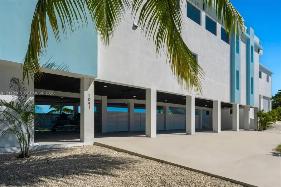 Modern multi-level exterior featuring white stucco finish, covered parking area, concrete driveway, horizontal slat privacy fencing, and recessed lighting Modern multi-level exterior featuring white stucco finish, covered parking area, concrete driveway, horizontal slat privacy fencing, and recessed lighting