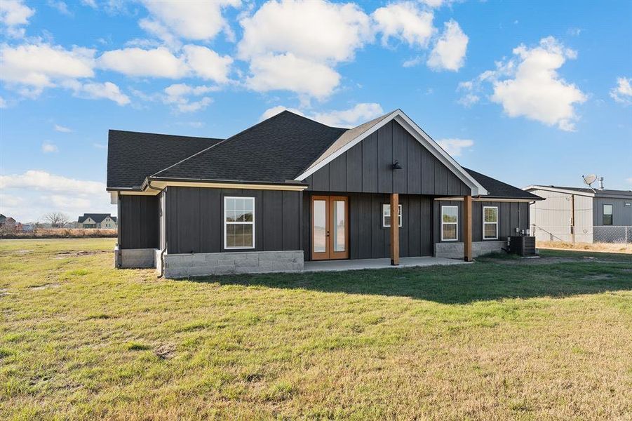 View of front of home featuring a front yard, board and batten siding, roof with shingles, and french doors