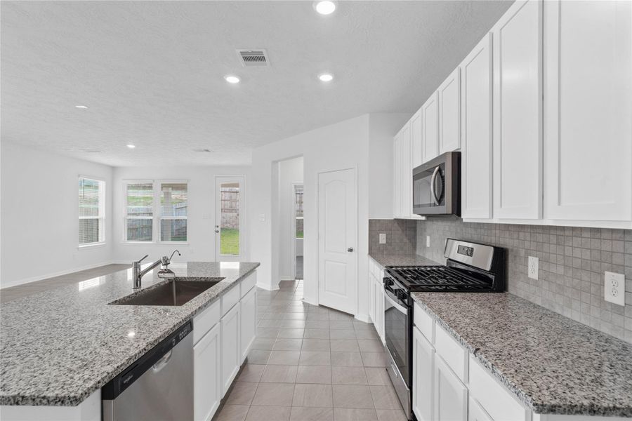 This bright, open kitchen is a chef's delight, complete with a large island, granite countertops, white Woodmont Dakota cabinets, Whirlpool stainless steel appliances, and modern Daltile backsplash.