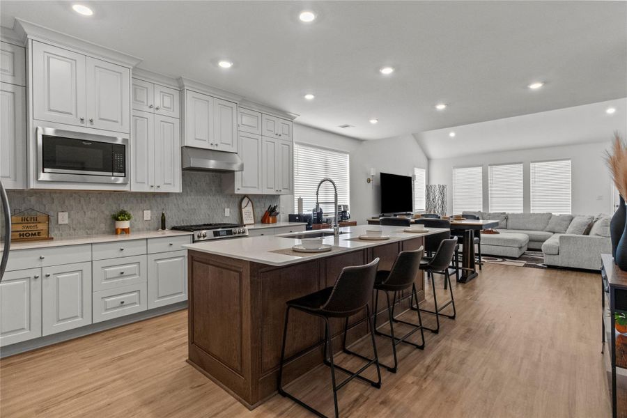 Bright and spacious open-concept kitchen and living area featuring sleek white cabinetry, a large central island with seating, and modern stainless steel appliances. The adjacent living room offers ample natural light and a cozy seating arrangement, perfect for entertaining or relaxing. Bright and spacious open-concept kitchen and living area featuring sleek white cabinetry, a large central island with seating, and modern stainless steel appliances. The adjacent living room offers ample natural light and a cozy seating arrangement, perfect for entertaining or relaxing.