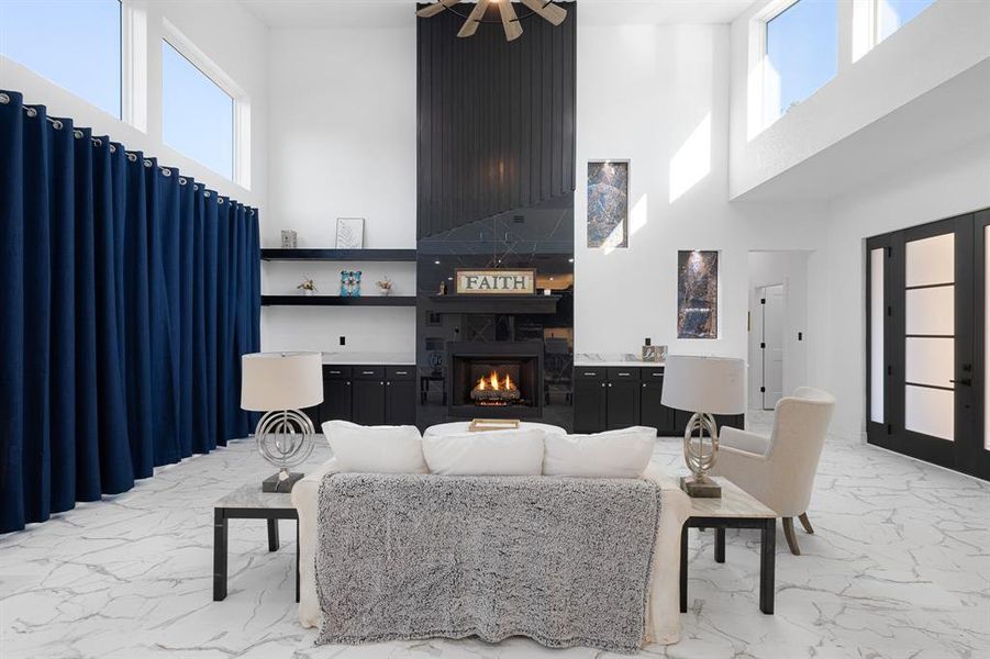 Living area with marble look tiles, a fireplace, a towering ceiling, french doors, and a ceiling fan