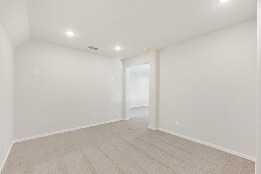 Empty bedroom with white walls, beige carpet, recessed lighting, and open doorway to hallway Empty bedroom with white walls, beige carpet, recessed lighting, and open doorway to hallway