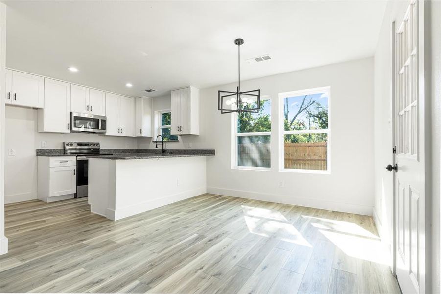 Kitchen with white cabinets, stainless steel appliances, a peninsula, dark stone countertops, and a chandelier