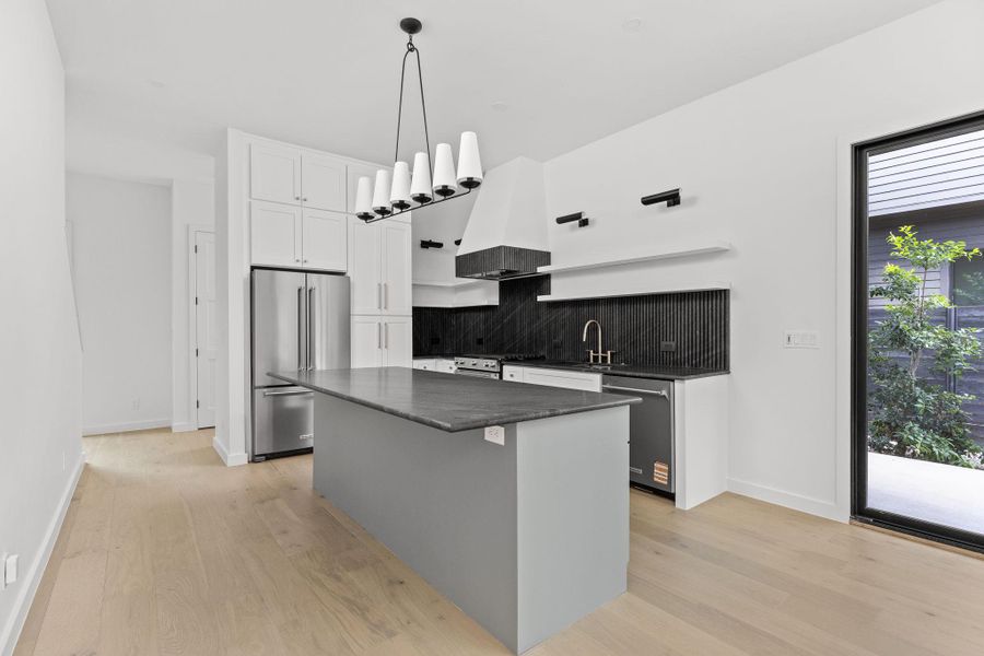 Kitchen with stainless steel appliances, wall chimney range hood, light wood-style flooring, and tasteful backsplash
