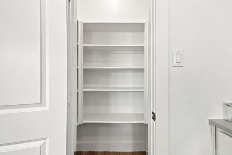 Convenient walk-in pantry with built-in shelving providing generous storage adjacent to the kitchen. Convenient walk-in pantry with built-in shelving providing generous storage adjacent to the kitchen.