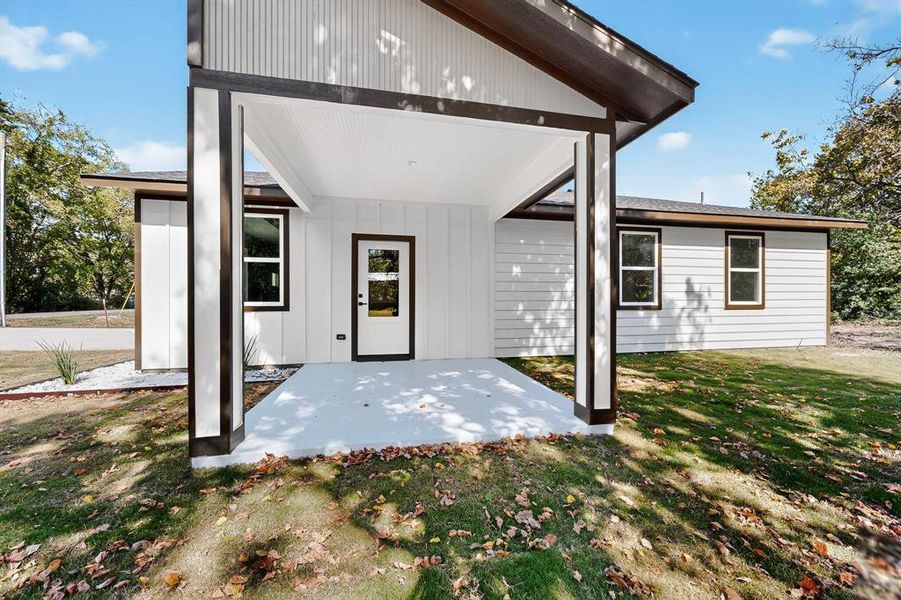 Entrance to property with a patio area, a yard, and board and batten siding Entrance to property with a patio area, a yard, and board and batten siding