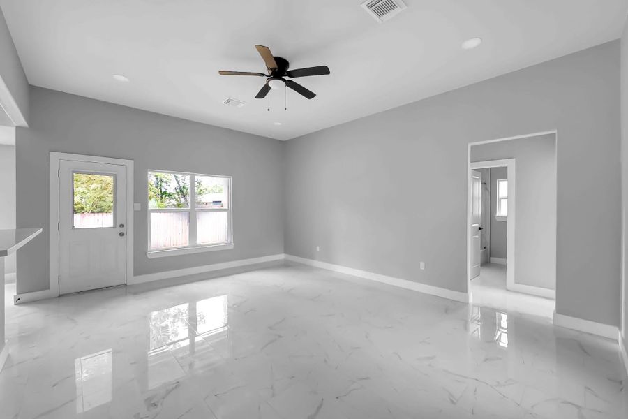 This photo showcases a spacious, bright living area with large windows, a ceiling fan, and sleek marble flooring. The neutral gray walls provide a modern and clean look, and there's a door leading outside, enhancing natural light.