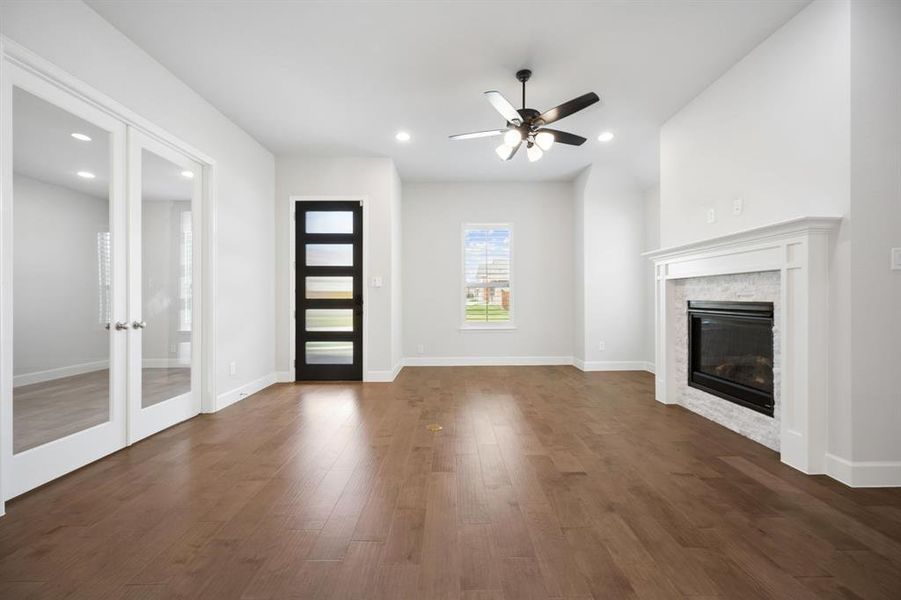 Spacious living area featuring hardwood flooring, a contemporary fireplace with a white mantel and stone surround, and recessed lighting