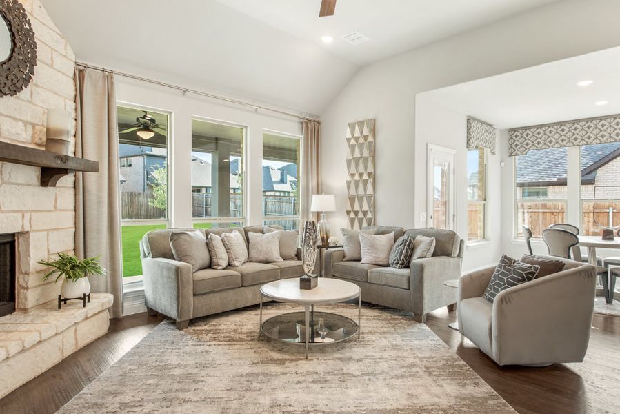 Living room with stone fireplace, gray sofas, hardwood floors, and large windows overlooking a backyard patio.