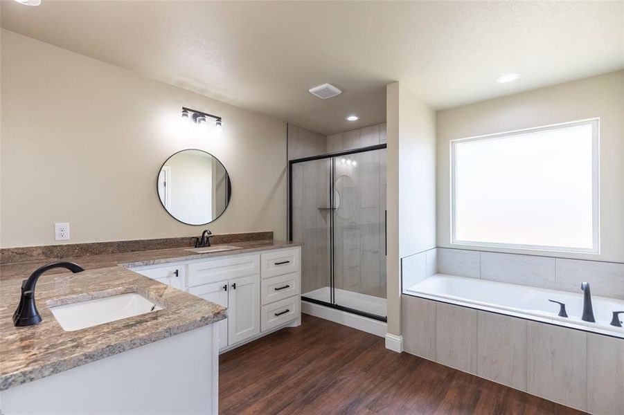 Bathroom featuring a dual vanity with undermount sinks and stone countertops, white cabinetry, a walk-in shower with a glass enclosure, a built-in soaking tub, and wood-finish flooring
