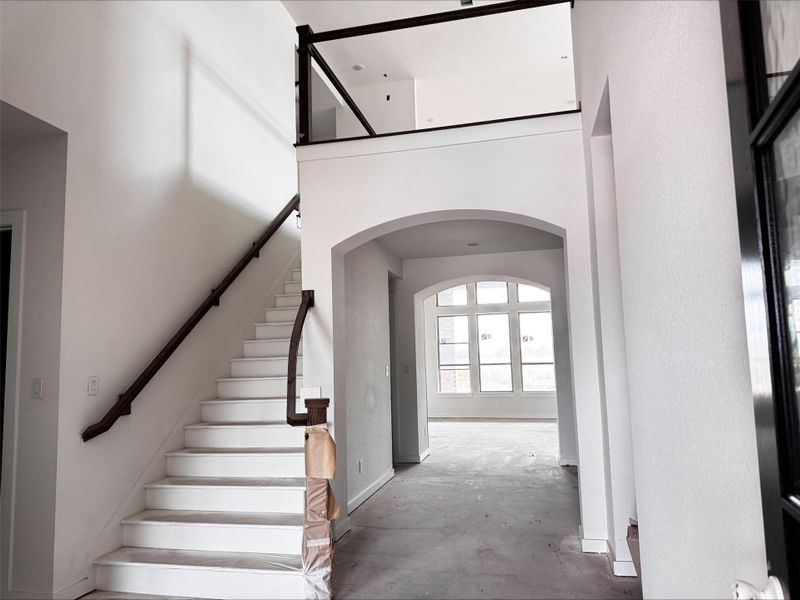 A bright, welcoming entry features a graceful staircase, soaring ceilings, and an elegant arched opening that creates an inviting sense of arrival.