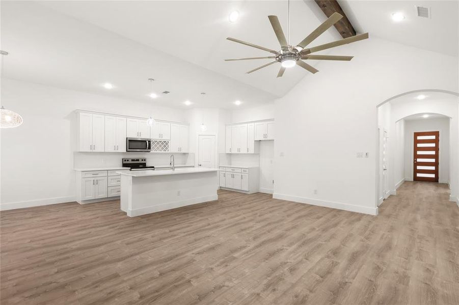 Kitchen featuring white cabinetry, stainless steel appliances, light hardwood / wood-style flooring, high vaulted ceiling, and an island with sink