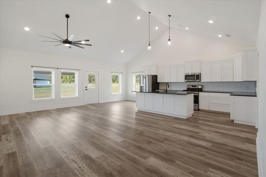 Kitchen with open floor plan, high vaulted ceiling, tasteful backsplash, dark countertops, and white cabinets