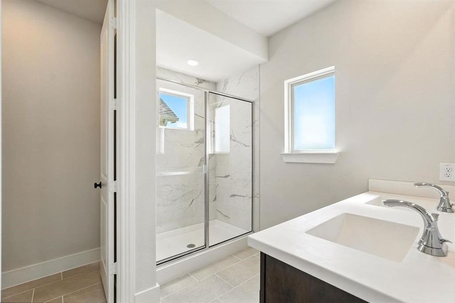 Bathroom with a marble finish shower, vanity, and light tile patterned flooring Bathroom with a marble finish shower, vanity, and light tile patterned flooring