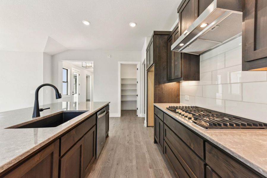 Kitchen with dark brown cabinetry, exhaust hood, light stone countertops, recessed lighting, and light wood-type flooring Kitchen with dark brown cabinetry, exhaust hood, light stone countertops, recessed lighting, and light wood-type flooring