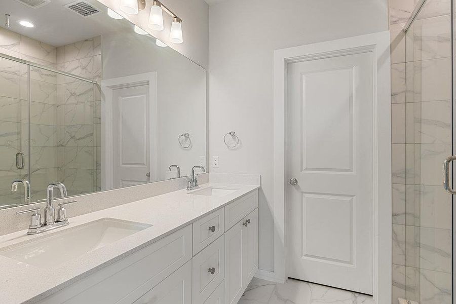 Bathroom with light marble finish flooring, a marble finish shower, and double vanity