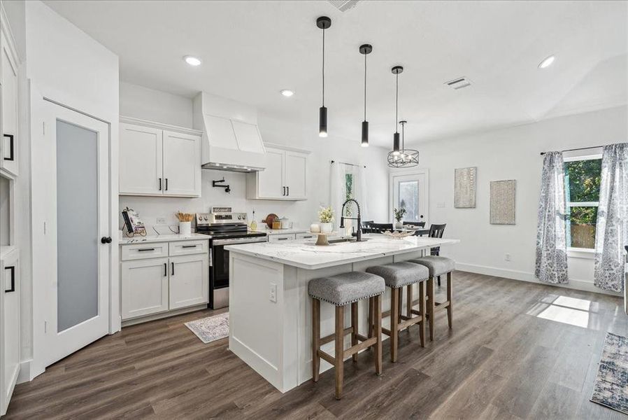 Kitchen with stainless steel electric stove, custom exhaust hood, a kitchen island with sink, and white cabinets