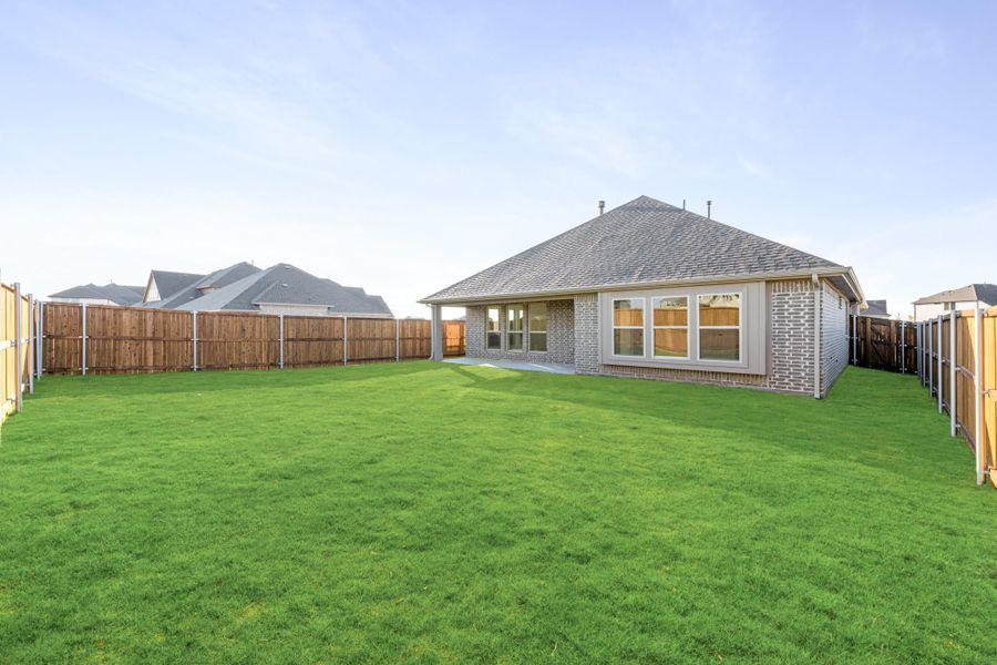 Backyard of brick home with large green lawn, wood privacy fence, and small concrete patio Backyard of brick home with large green lawn, wood privacy fence, and small concrete patio