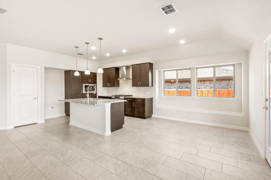 Open kitchen with dark wood cabinets, granite island, pendant lights, and tile floors open to living area Open kitchen with dark wood cabinets, granite island, pendant lights, and tile floors open to living area