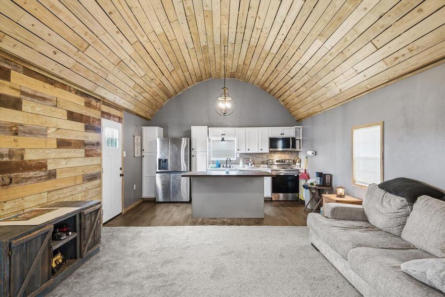 Livingroom featuring open floor plan, white cabinets, stainless steel appliances, a kitchen island, and a vaulted wooden ceiling