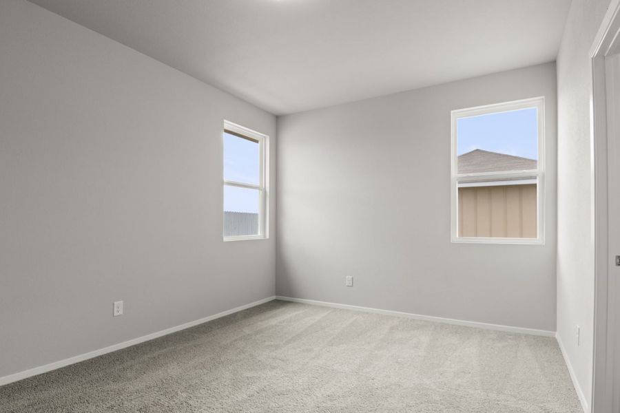 Image of primary bedroom with tan carpet, grey walls and two windows