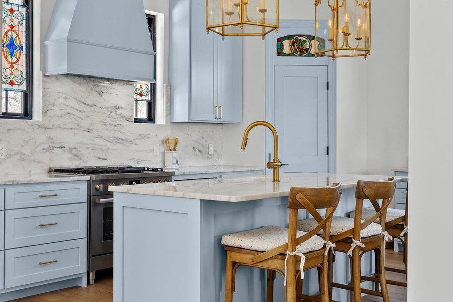 Kitchen with a kitchen bar, high end stove, light stone countertops, wood finished floors, and a center island with sink