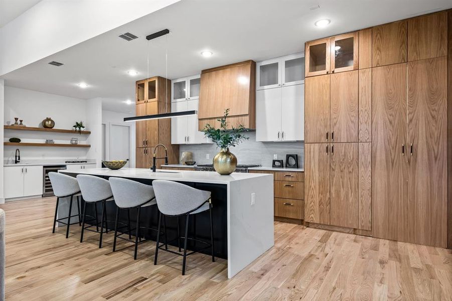 Kitchen featuring a kitchen island with sink, white cabinets, beverage cooler, and light wood-type flooring