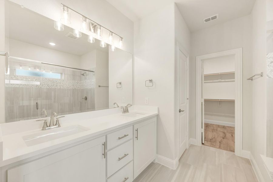 Ensuite bathroom with double vanity, large mirror, walk-in shower, and open walk-in closet doorway