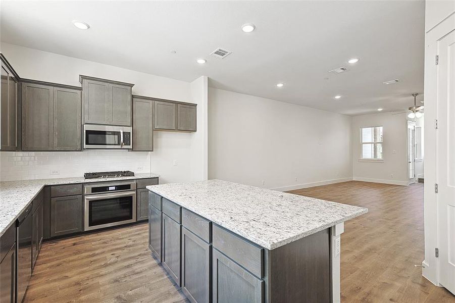 Kitchen featuring ceiling fan, a center island, stainless steel appliances, light stone counters, and light hardwood / wood-style flooring