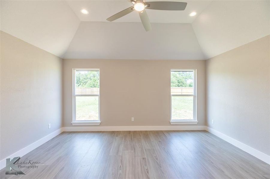 Spare room featuring vaulted ceiling, plenty of natural light, light wood-style flooring, a ceiling fan, and recessed lighting