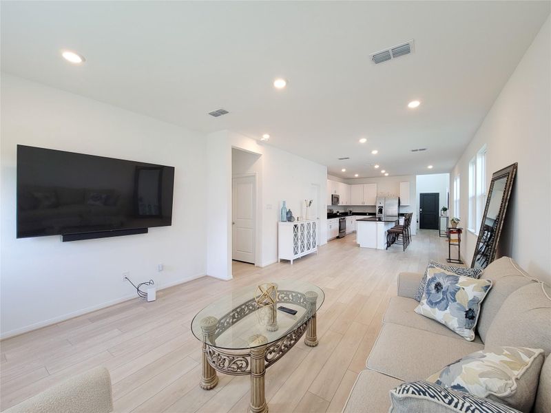 This spacious open-concept living area features a modern kitchen with sleek white cabinets and a large island. Ample natural light streams through multiple windows, enhancing the bright and inviting atmosphere.