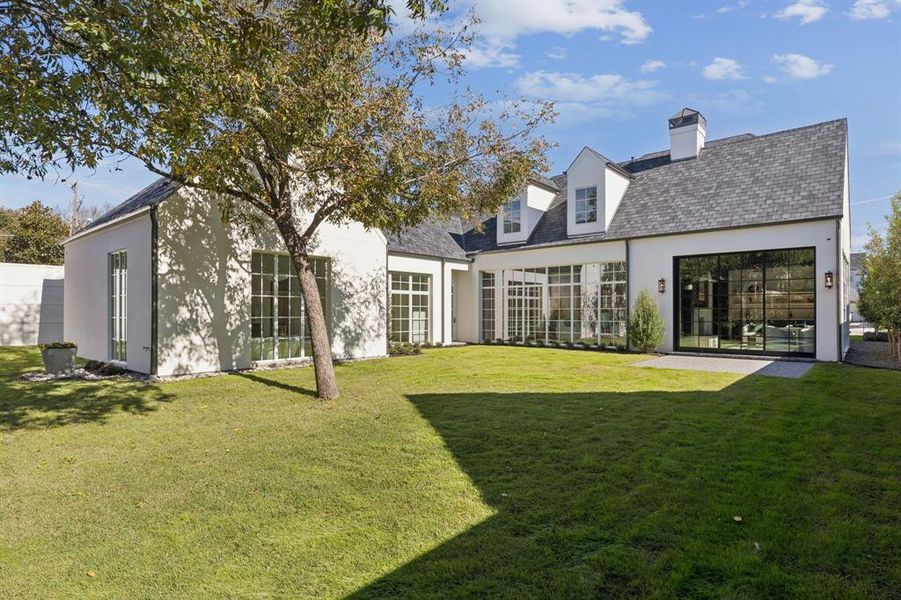 Back of property with stucco siding, a lawn, and a chimney