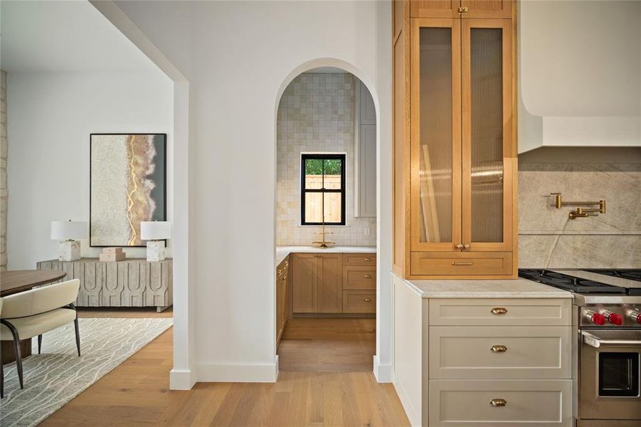 Kitchen with premium stove, light wood finished floors, decorative backsplash, and glass insert cabinets