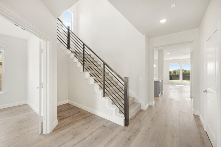 Bright entryway with staircase featuring metal railing and light hardwood floors leading to open living area