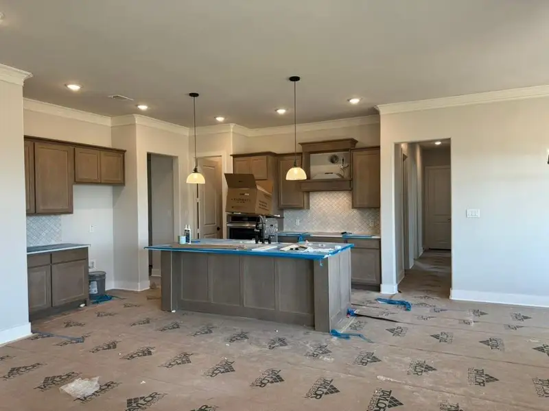 Kitchen featuring a kitchen island with sink, decorative backsplash, wood finish cabinetry, crown molding, and oven