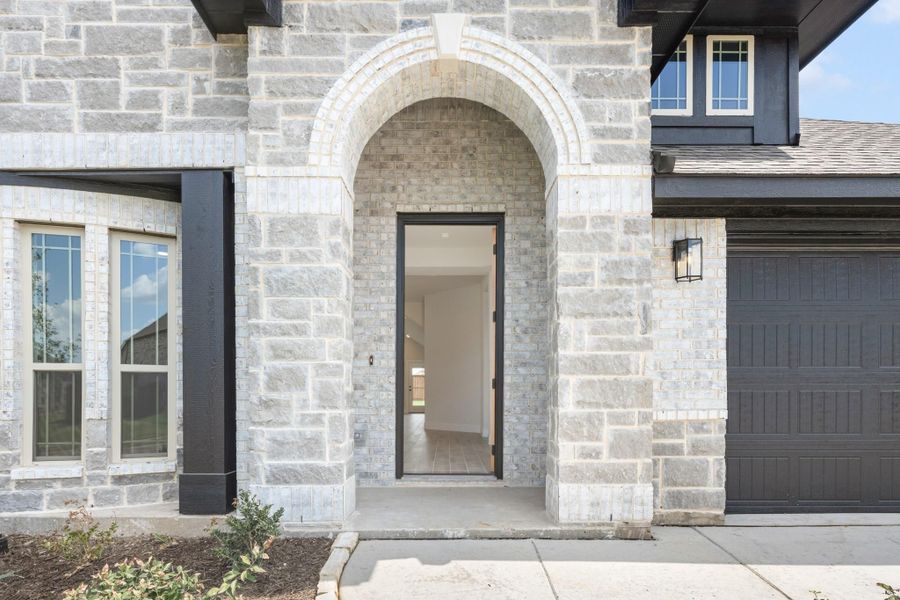 Stone home entrance with arched doorway, dark front door, and attached garage visible on right