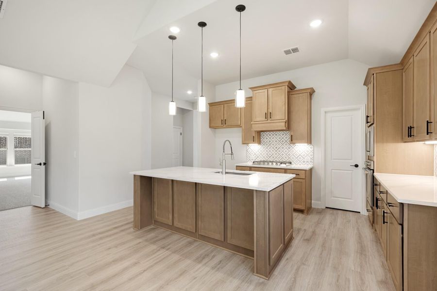 Kitchen with large center island, light wood cabinets, white countertops, and pendant lights over light wood floors