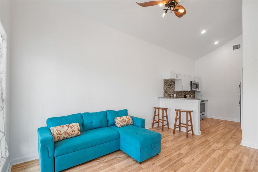 The entry is a bright, contemporary space featuring vinyl plank floors that continue throughout the home, and a white kitchen with bar seating. The room has high ceilings with recessed lighting and a ceiling fan, creating an open and airy feel.