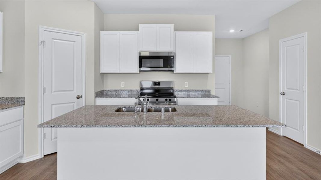 Kitchen featuring a central island with an integrated sink, white cabinetry, a stainless steel microwave, a stainless steel gas range, and wood-finish flooring