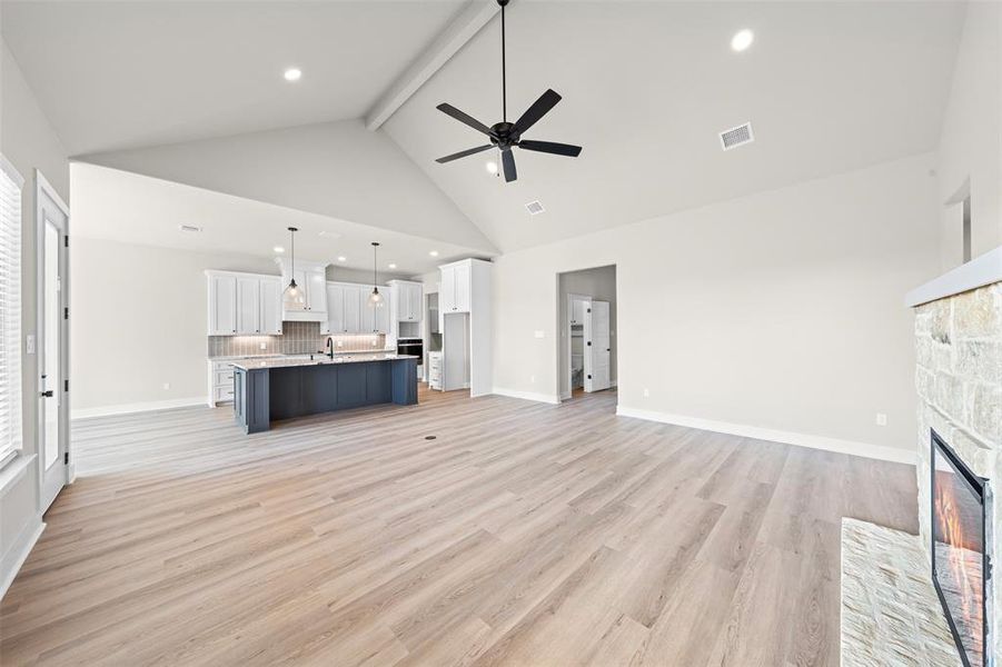 Unfurnished living room with a stone fireplace, light wood-type flooring, beam ceiling, high vaulted ceiling, and recessed lighting
